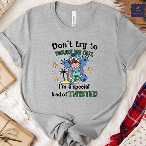 May include: A gray t-shirt featuring a graphic of a blue cartoon character with the text "Don't try to FIGURE ME OUT, I'm a special kind of TWISTED." The character is wearing a Hawaiian shirt and is surrounded by stars and palm trees.