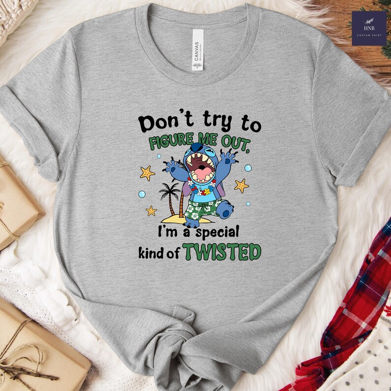 May include: A gray t-shirt featuring a graphic of a blue cartoon character with the text "Don't try to FIGURE ME OUT, I'm a special kind of TWISTED." The character is wearing a Hawaiian shirt and is surrounded by stars and palm trees.
