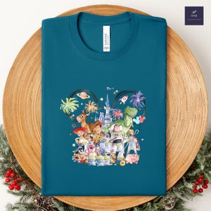 May include: Teal t-shirt featuring a colorful graphic of Disney characters, including Woody, Buzz Lightyear, and Rex. The design is set within a Mickey Mouse ear outline, with the word "CANVAS" printed on the shirt.