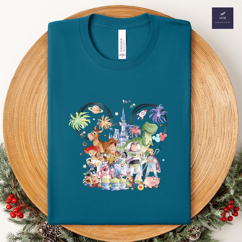 May include: Teal t-shirt featuring a colorful graphic of Disney characters, including Woody, Buzz Lightyear, and Rex. The design is set within a Mickey Mouse ear outline, with the word "CANVAS" printed on the shirt.