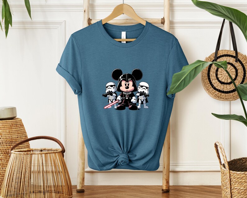 Pu&ograve; includere: Una maglietta color verde acqua con una grafica a cartoni animati di Topolino nei panni di Darth Vader, affiancato da due Stormtrooper. Il design include una spada laser rossa. La maglietta &egrave; annodata in basso.