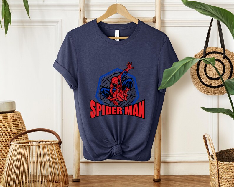 May include: Navy blue t-shirt featuring a Spider-Man graphic. The design includes a red and blue Spider-Man figure within a blue web-like hexagon, with the words "SPIDER MAN" in red. The shirt is knotted at the bottom.