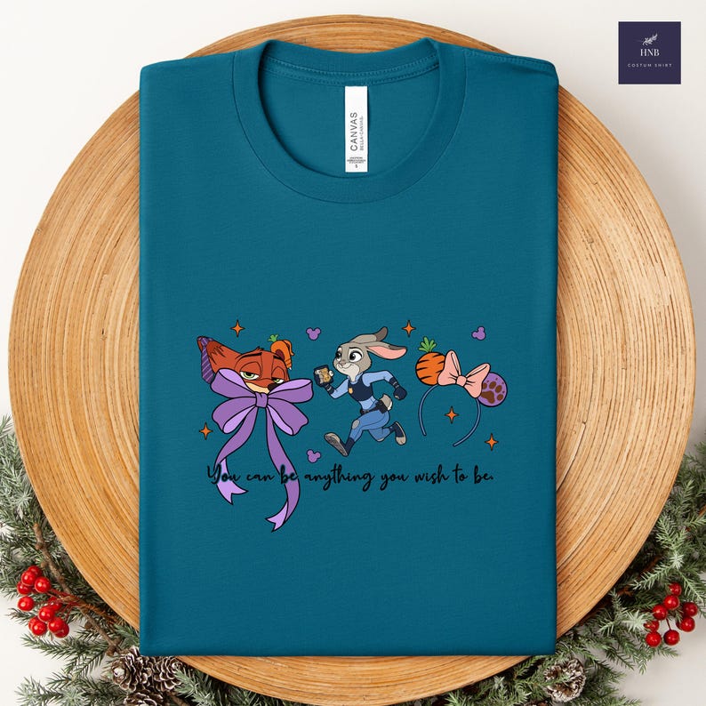 May include: Teal t-shirt featuring cartoon characters and the text "You can be anything you wish to be." The design includes a fox with a purple bow, a running rabbit, and a carrot-shaped headband with a pink bow.