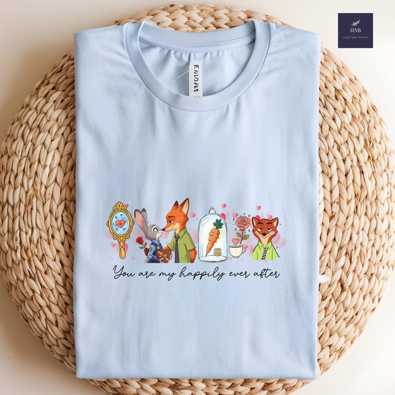 May include: Light blue t-shirt featuring a cartoon design with characters from Zootopia. The design includes Judy Hopps, Nick Wilde, and other characters, along with the text "You are my happily ever after."