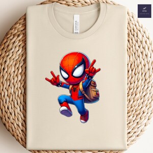 Puede incluir: Camiseta beige con una ilustraci&oacute;n de dibujos animados de Spider-Man. El personaje est&aacute; en una pose din&aacute;mica, vistiendo su traje rojo y azul y una mochila. La camiseta tiene cuello redondo y una etiqueta "Canvas".