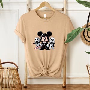 Pu&ograve; includere: T-shirt color cachi con grafica a cartoni animati di Topolino vestito da Darth Vader, affiancato da due Stormtrooper. Il design include una spada laser rossa ed &egrave; centrato sul davanti della maglietta.