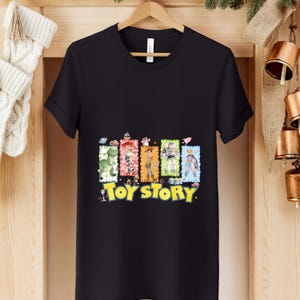 Puede incluir: Camiseta negra con un gr&aacute;fico colorido de personajes de la pel&iacute;cula animada "Toy Story". El dise&ntilde;o incluye un dinosaurio, una vaquera, un vaquero, un guardabosques espacial y el t&iacute;tulo de la pel&iacute;cula en amarillo.