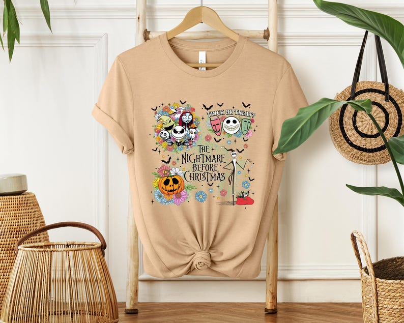 May include: Tan t-shirt featuring a colorful graphic from "The Nightmare Before Christmas." The design includes Jack Skellington, Sally, Zero, and other characters, along with the text "Trick or Treat" and "The Nightmare Before Christmas."