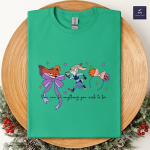 May include: A green t-shirt featuring cartoon characters from Zootopia. The design includes Nick Wilde with a purple bow, Judy Hopps in a police uniform, and a carrot-shaped headband. The text "You can be anything you wish to be" is also included.