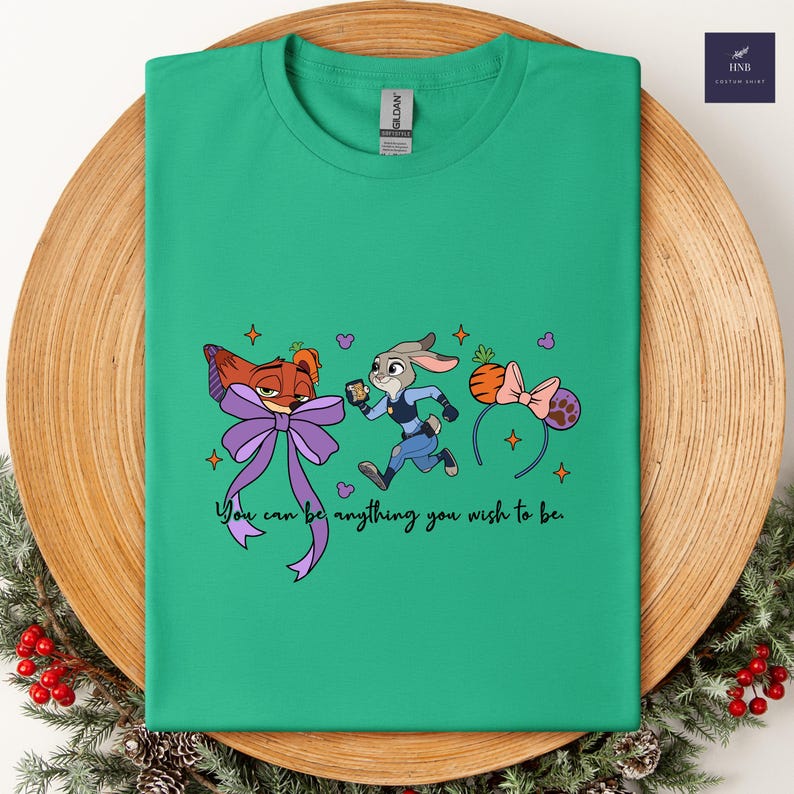 May include: A green t-shirt featuring cartoon characters from Zootopia. The design includes Nick Wilde with a purple bow, Judy Hopps in a police uniform, and a carrot-shaped headband. The text "You can be anything you wish to be" is also included.