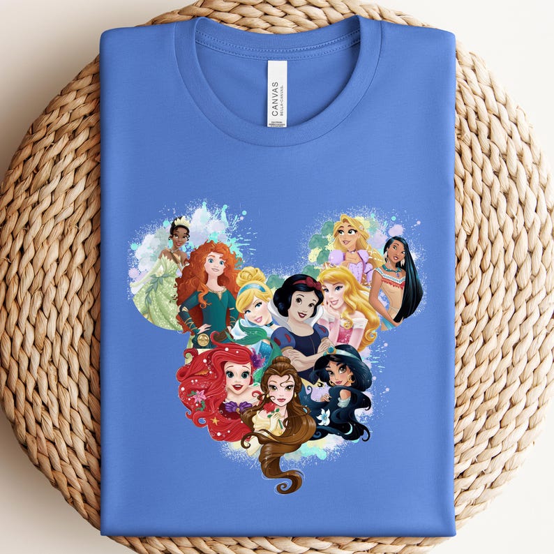 K&ouml;nnte beinhalten: Blaues T-Shirt mit einer farbenfrohen Grafik von Disney-Prinzessinnen, die in Form eines Mickey Mouse-Kopfes angeordnet sind. Die Prinzessinnen sind Ariel, Schneewittchen und Belle. Das Shirt ist aus weichem Material.