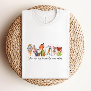 May include: White t-shirt with a watercolor illustration featuring characters from a popular animated movie. The design includes a mirror, a rabbit, a fox, a carrot in a glass dome, and a rose. The text "You are my happily ever after" is written below the illustration.