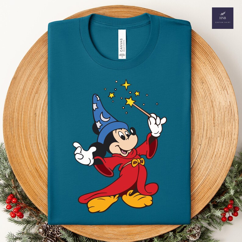 Puede incluir: Camiseta de color turquesa con un dise&ntilde;o de Mickey Mouse de dibujos animados como mago. Mickey lleva un sombrero azul y una t&uacute;nica roja, sosteniendo una varita con estrellas. La camiseta tiene una etiqueta "Canvas".