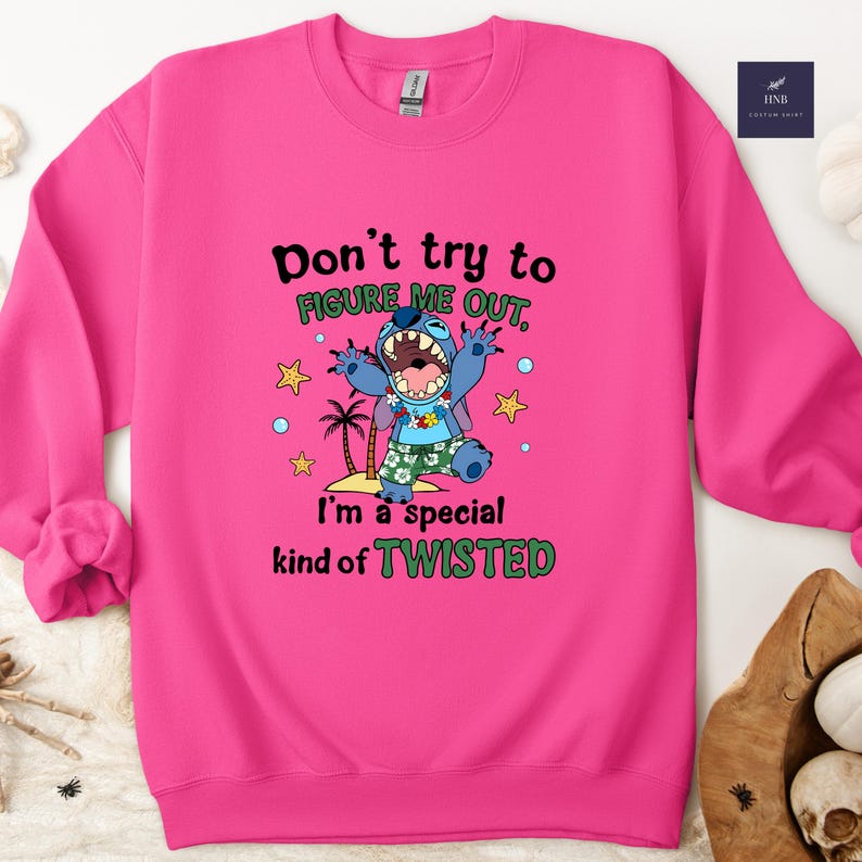 May include: A vibrant pink sweatshirt featuring a graphic of a blue cartoon character with the text "Don't try to FIGURE ME OUT, I'm a special kind of TWISTED." The design includes palm trees and stars.