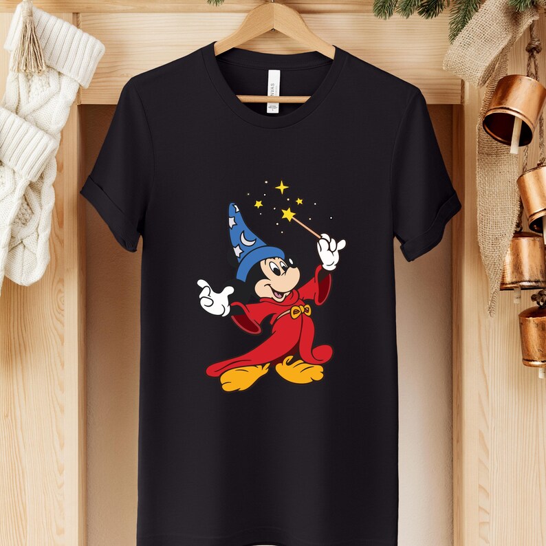 Puede incluir: Camiseta negra con una ilustraci&oacute;n de dibujos animados de Mickey Mouse como hechicero. Mickey lleva un sombrero azul, una t&uacute;nica roja y zapatos amarillos, sosteniendo una varita con estrellas. El dise&ntilde;o est&aacute; centrado en la camiseta.