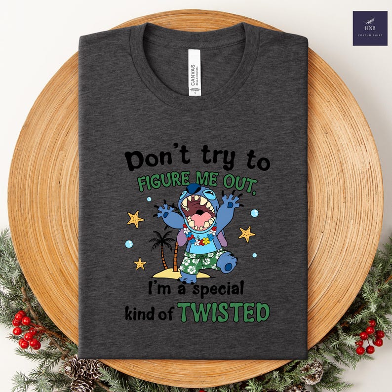 May include: Dark gray t-shirt featuring a cartoon character with the text "Don't try to figure me out, I'm a special kind of twisted." The character is blue with a floral lei and tropical shorts. The shirt is folded.