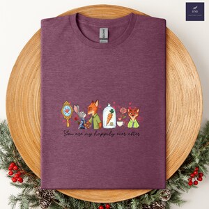 May include: A maroon t-shirt featuring a cartoon design with characters from a popular animated movie. The design includes a mirror, a rabbit, a fox, a carrot, a rose, and a teacup. The text "You are my happily ever after" is below the design.