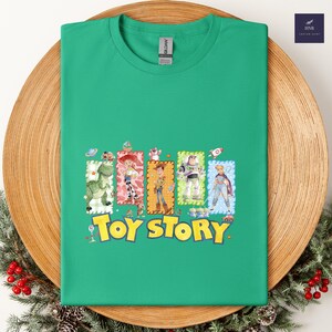 Puede incluir: Una camiseta verde con un gr&aacute;fico colorido de personajes de la pel&iacute;cula animada "Toy Story". El dise&ntilde;o incluye im&aacute;genes de Woody, Buzz Lightyear y otros personajes, con las palabras "Toy Story" en amarillo.