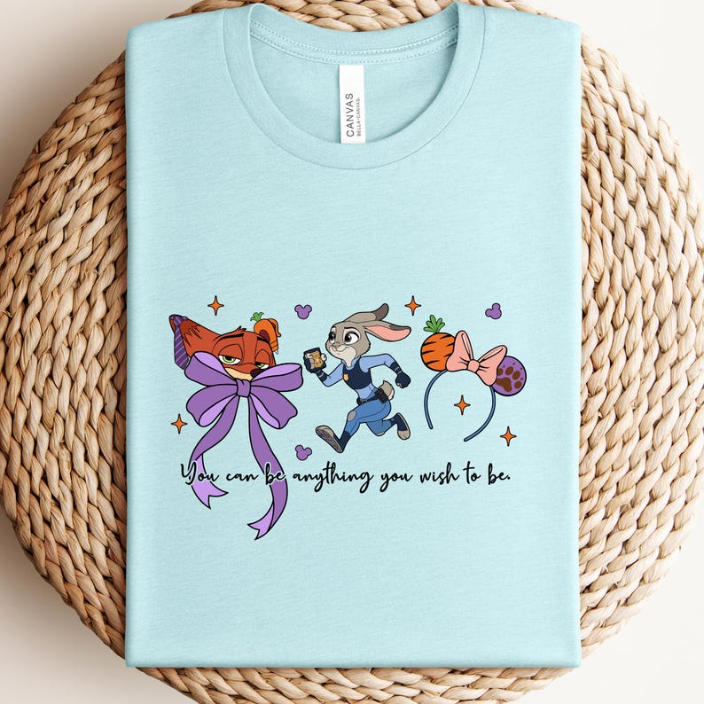 May include: Light blue t-shirt featuring cartoon characters and the text "You can be anything you wish to be." The design includes a fox with a purple bow, a rabbit in a police uniform, and a carrot headband.