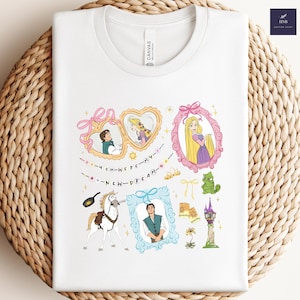 May include: White t-shirt featuring a colorful graphic design with characters and elements from a fairytale. The design includes framed portraits, a horse, and the text "YOU WERE MY NEW DREAM."
