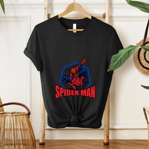 May include: Black t-shirt featuring a Spider-Man graphic. The design includes a red and blue Spider-Man figure within a blue web-like frame, with the words "SPIDER MAN" in red below.