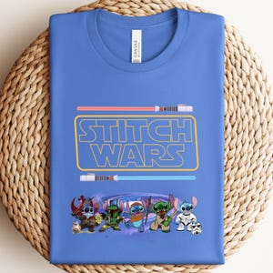 Puede incluir: Una camiseta azul con el texto "Stitch Wars" en amarillo y un gr&aacute;fico de personajes de Stitch de la pel&iacute;cula de Disney Lilo & Stitch. Los personajes sostienen sables de luz y est&aacute;n en un fondo de galaxia.
