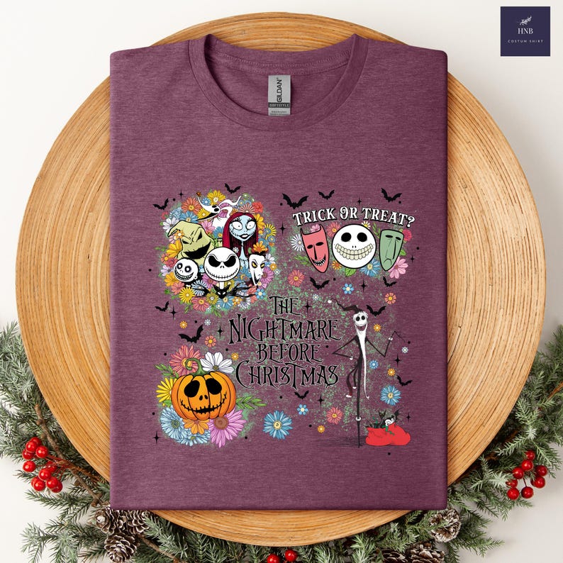 May include: A maroon t-shirt featuring a colorful graphic from "The Nightmare Before Christmas." The design includes Jack Skellington, Sally, Zero, and other characters, along with the text "Trick or Treat?" and "The Nightmare Before Christmas."
