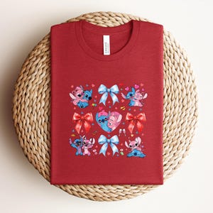 May include: A red t-shirt featuring a graphic design of the characters Stitch and Angel, with bows and hearts. The design includes the word "Canvas" on the tag.