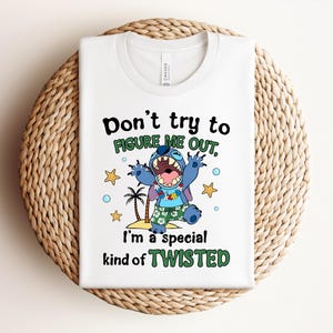 May include: White t-shirt featuring a cartoon character with the text "Don't try to figure me out, I'm a special kind of TWISTED." The character is blue with a wide open mouth, wearing a Hawaiian shirt and shorts. Palm trees and stars are also featured.