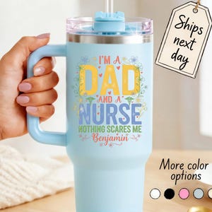 May include: A light blue insulated tumbler with a handle and a straw. The tumbler has the text "I'M A DAD AND A NURSE NOTHING SCARES ME Benjamin" in yellow, blue, and green. The tumbler has a clear lid and a light blue handle.