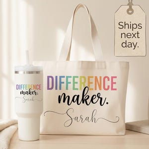 May include: A white canvas tote bag and a matching white insulated tumbler with a straw. Both items feature the colorful text "DIFFERENCE maker." and the name "Sarah" in black script. The tote has two handles and the tumbler has a lid.