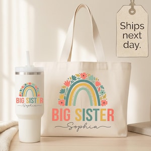 May include: A cream-colored canvas tote bag and a matching white stainless steel tumbler with a straw. Both items feature a colorful rainbow graphic adorned with flowers, the text "BIG SISTER," and the name "Sophia" in a cursive script font.