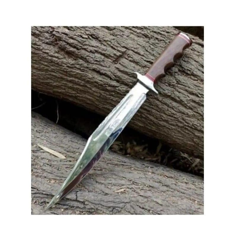 K&ouml;nnte beinhalten: Ein silbernes Messer mit einem braunen Holzgriff und einer roten Spitze. Das Messer liegt auf einem St&uuml;ck Holz.