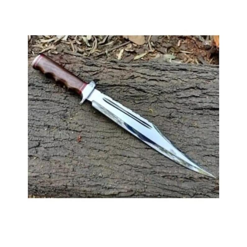 K&ouml;nnte beinhalten: Ein silberfarbenes Jagdmesser mit einem braunen Holzgriff. Das Messer liegt auf einem St&uuml;ck Holz.