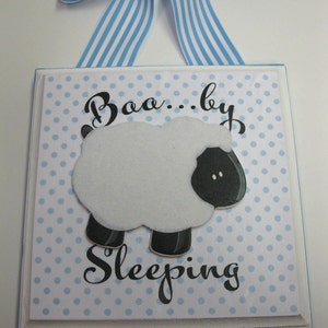 May include: A white wooden sign with blue polka dots and a black and white sheep illustration. The sign says "Baa...by Sleeping".