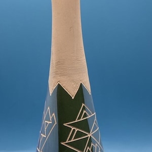 Può includere: Un vaso alto in ceramica con collo beige chiaro e corpo blu e verde. Il corpo presenta disegni geometrici a linee bianche. Il vaso ha una forma sottile e allungata, su sfondo blu.