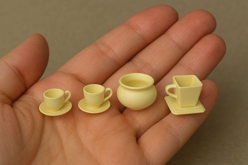 May include: A collection of miniature, pale yellow teacups, saucers, and a small pot are arranged in a hand. The set includes two traditional teacups with saucers, a small pot, and a square teacup with a matching square saucer.