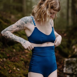 May include: A two-piece swimsuit in a deep blue hue. The top is a V-neck style with adjustable straps, and the high-waisted bottoms offer full coverage. The fabric has a smooth, matte finish, and the design is simple and elegant.