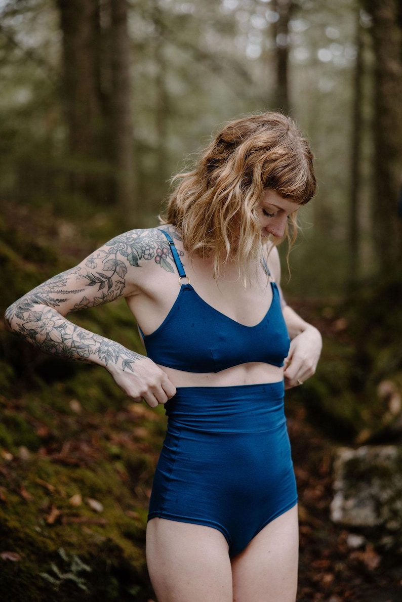 May include: A two-piece swimsuit in a deep blue hue. The top is a V-neck style with adjustable straps, and the high-waisted bottoms offer full coverage. The fabric has a smooth, matte finish, and the design is simple and elegant.
