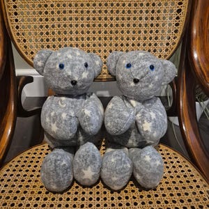 May include: Two grey plush teddy bears with white stars and blue eyes sitting on a wicker chair.