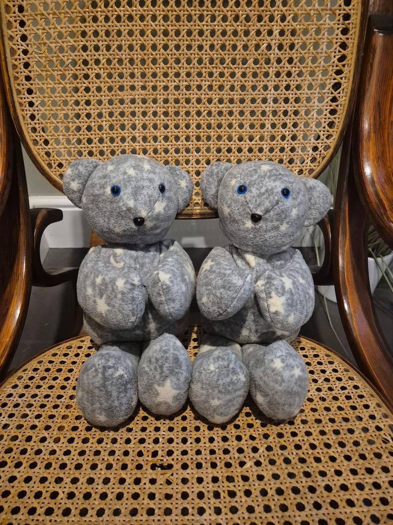 May include: Two grey plush teddy bears with white stars and blue eyes sitting on a wicker chair.