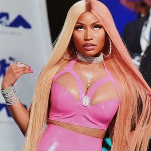 May include: A photograph of a person in a pink outfit, with long blonde and pink hair. The person is wearing a pink top and matching trousers. The image includes a signature and a small heart.