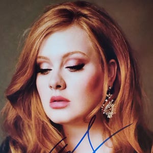 Puede incluir: Retrato de una mujer con cabello castaño rojizo y una firma. Tiene tez clara, maquillaje con tonos rosados. Su cabello está peinado en ondas sueltas. Lleva un top negro y pendientes grandes y ornamentados.