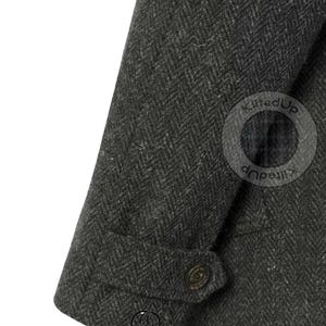 Puede incluir: Primer plano de una manga de chaqueta de tweed gris oscuro. La tela tiene un patr&oacute;n de espiga. Se ve un pu&ntilde;o abotonado y un peque&ntilde;o logotipo. La chaqueta parece ser parte de una colecci&oacute;n de ropa formal.