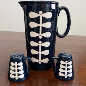 May include: A navy blue ceramic pitcher and two salt shakers with a white leaf design. The pitcher has a handle and is approximately 8 inches tall. The salt shakers are small and have handles.