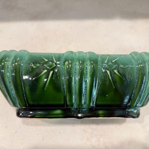 May include: A rectangular, glossy, green ceramic planter with a ribbed design. The planter has a dark green base and features star-like accents on the front. The planter is suitable for indoor or outdoor use.