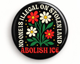 May include: A round black pin-back button featuring a central illustration of red and white flowers with green leaves. The text NO ONE IS ILLEGAL ON STOLEN LAND is arched around the top, and ABOLISH ICE is printed in red at the bottom.