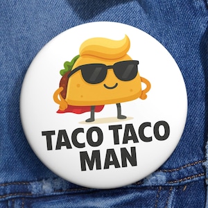 May include: A white badge featuring a cartoon taco character with sunglasses and a cape. The taco is yellow with a red cape and green lettuce. The text "TACO TACO MAN" is printed in bold black letters.