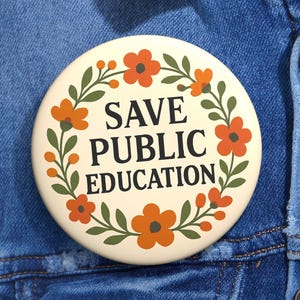 Puede incluir: Un botón redondo de color crema con el texto "SAVE PUBLIC EDUCATION" en negro, rodeado de flores naranjas y hojas verdes. El botón está prendido a una chaqueta vaquera azul.
