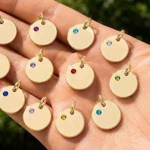 Puede incluir: Un conjunto de doce pequeños dijes circulares de metal en tono dorado, cada uno con una piedra preciosa redonda incrustada de un color diferente. Cada dije incluye una pequeña argolla en la parte superior y una superficie lisa y pulida.